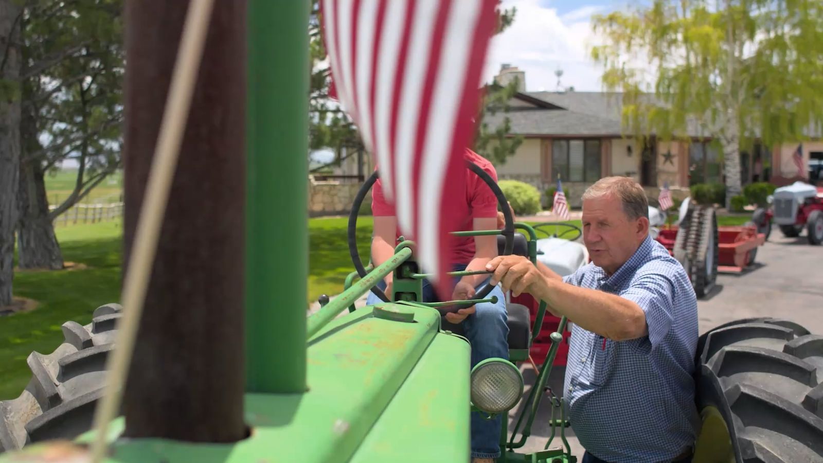 A man in a blue checked shirt reaches for the controls of a green vintage tractor